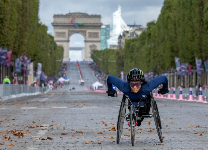 A female Paralympic wheelchair racer is competing in a marathon outdoors
